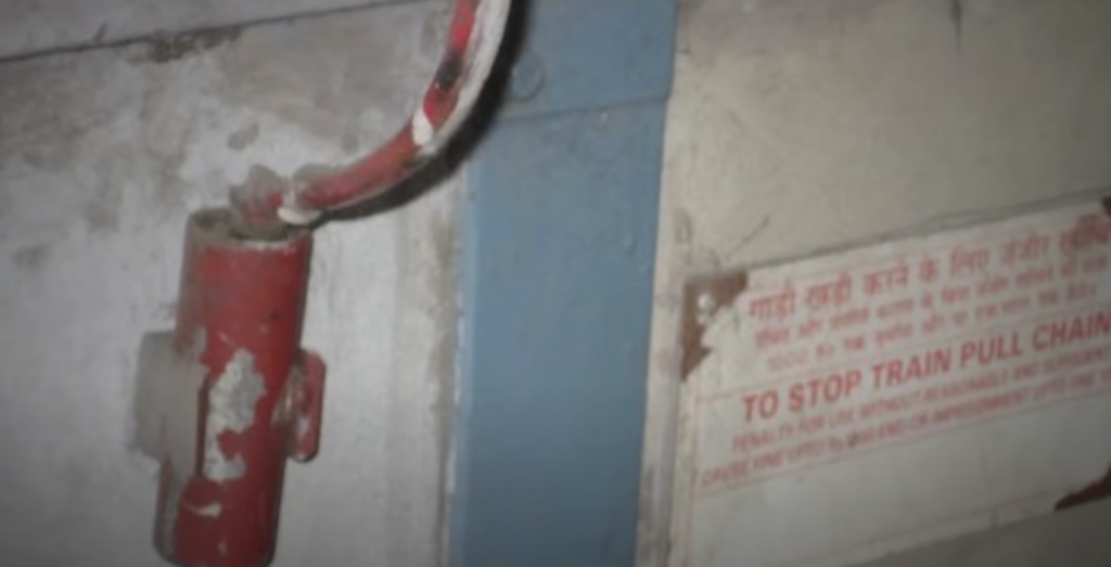 A red emergency chain inside a train compartment, designed for passenger safety. When pulled, this chain activates an alarm system, notifying the train driver and nearby railway police. Outside the compartment, a pressure valve releases with a loud noise, indicating the chain has been engaged. This safety feature allows for quick response in emergencies, enhancing passenger protection and reducing risks of potential incidents.